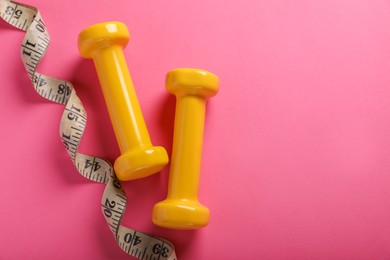 Measuring tape and dumbbells on pink background, flat lay with space for text. Weight control concept