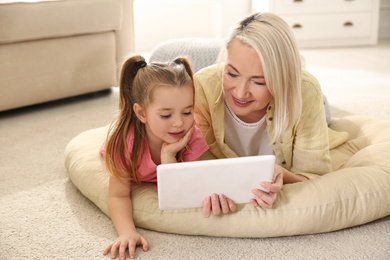 Photo of Mature woman and her little granddaughter with tablet at home