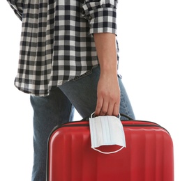 Photo of Woman with suitcase and protective mask on white background, closeup. Travelling during coronavirus pandemic