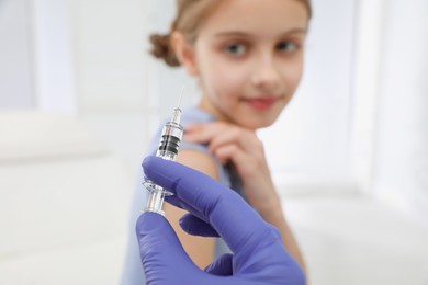 Doctor giving injection to little girl in hospital, focus on hand. Immunization concept