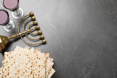 Photo of Stack of traditional matzos, red wine and menorah on grey table, flat lay. Space for text
