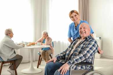 Nurse assisting elderly man in wheelchair at retirement home. Space for text