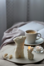 Beautiful body shaped candles and cup of hot drink on bench indoors