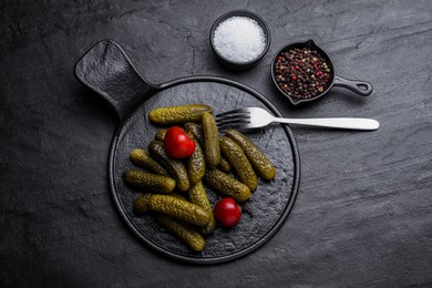 Photo of Serving board with pickled cucumbers and peppers on black table, flat lay