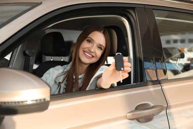 Beautiful woman with car key sitting in modern auto at dealership