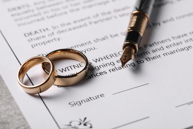 Marriage contract, fountain pen and golden wedding rings on table, closeup