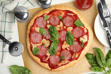 Pita pizza with pepperoni, cheese and basil on white wooden table, flat lay