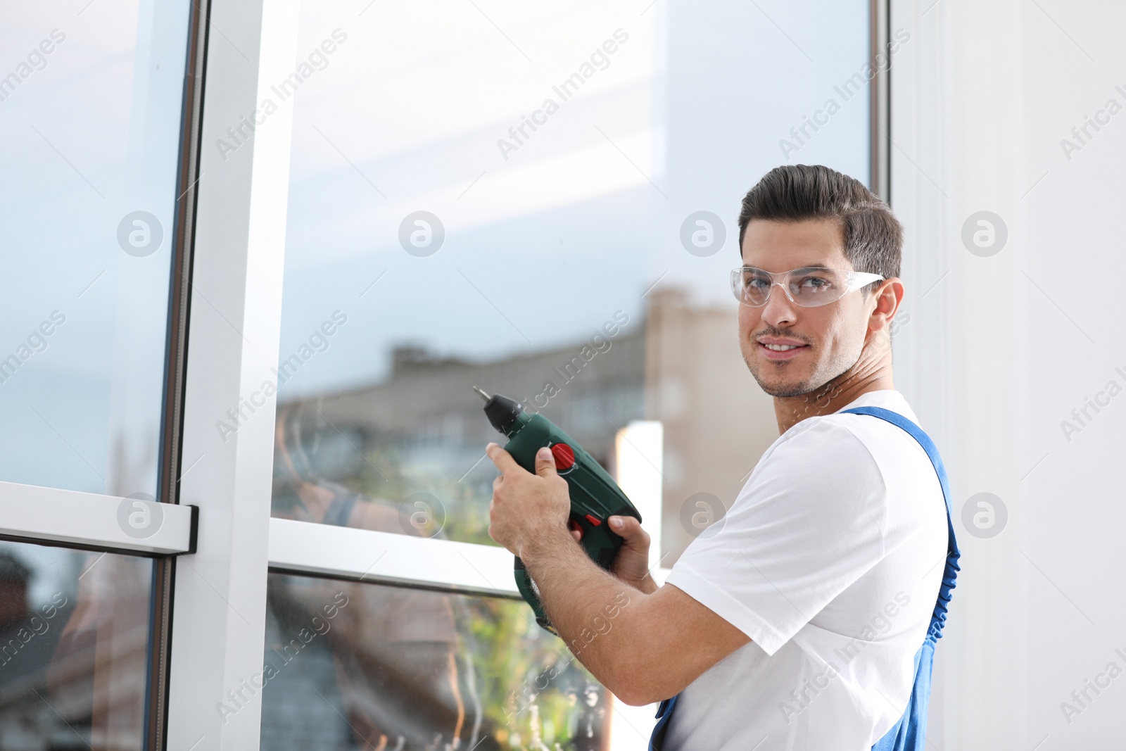 Photo of Construction worker repairing plastic window with electric screwdriver indoors