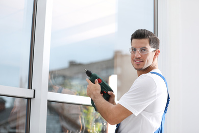 Construction worker repairing plastic window with electric screwdriver indoors