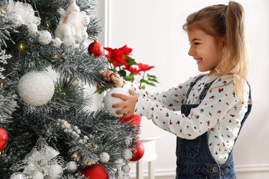 Photo of Cute little girl decorating Christmas tree at home