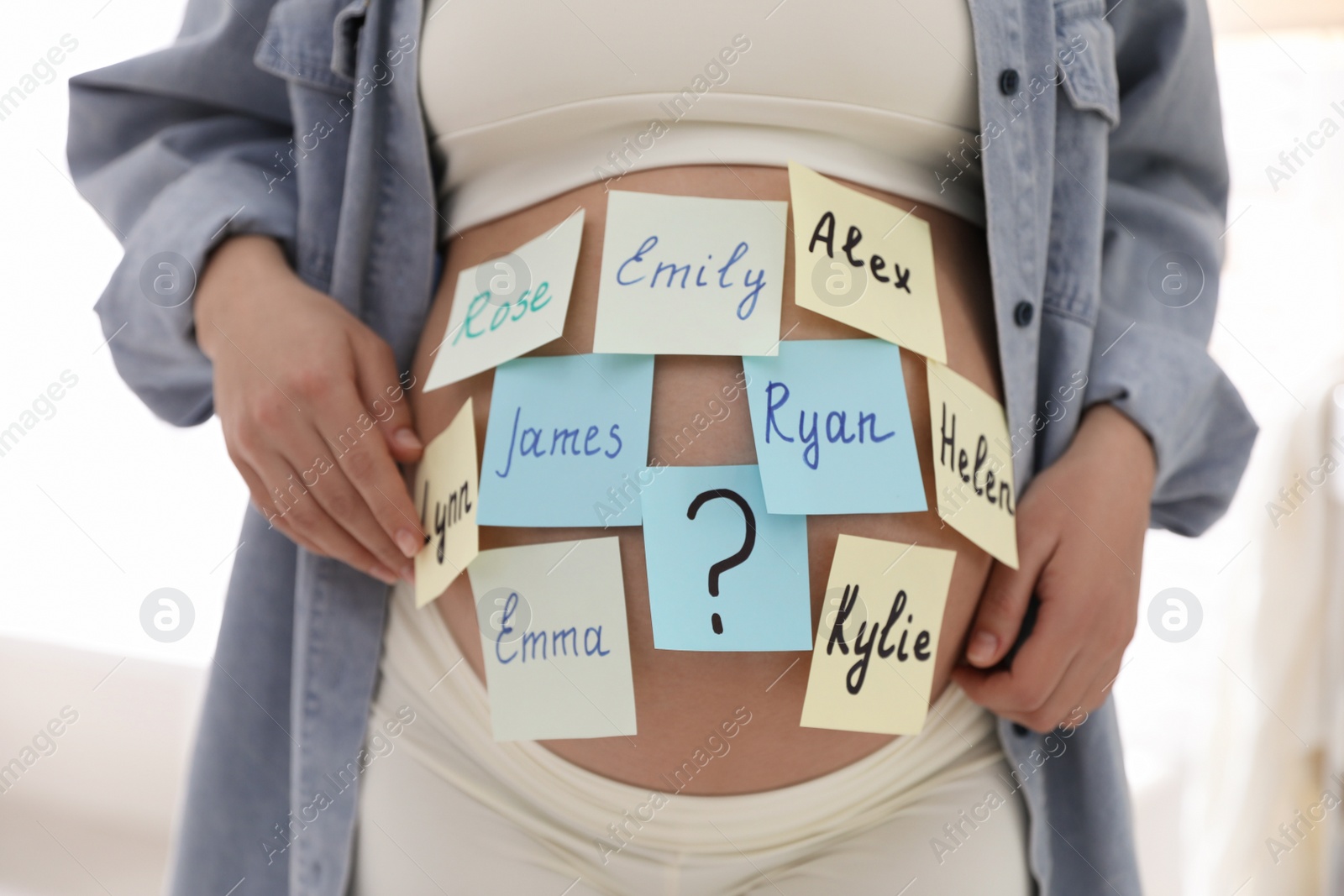 Photo of Pregnant woman with different baby names on belly indoors, closeup