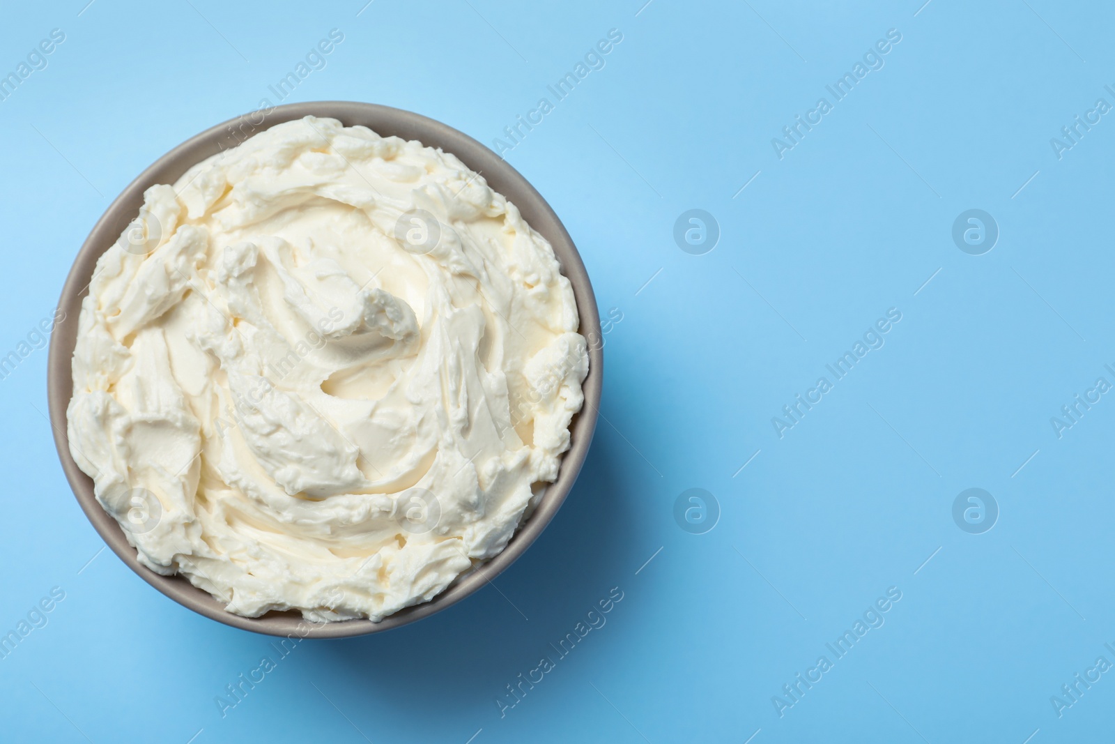 Photo of Bowl of tasty cream cheese on light blue background, top view. Space for text