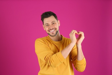 Portrait of handsome man making heart with his hands on color background