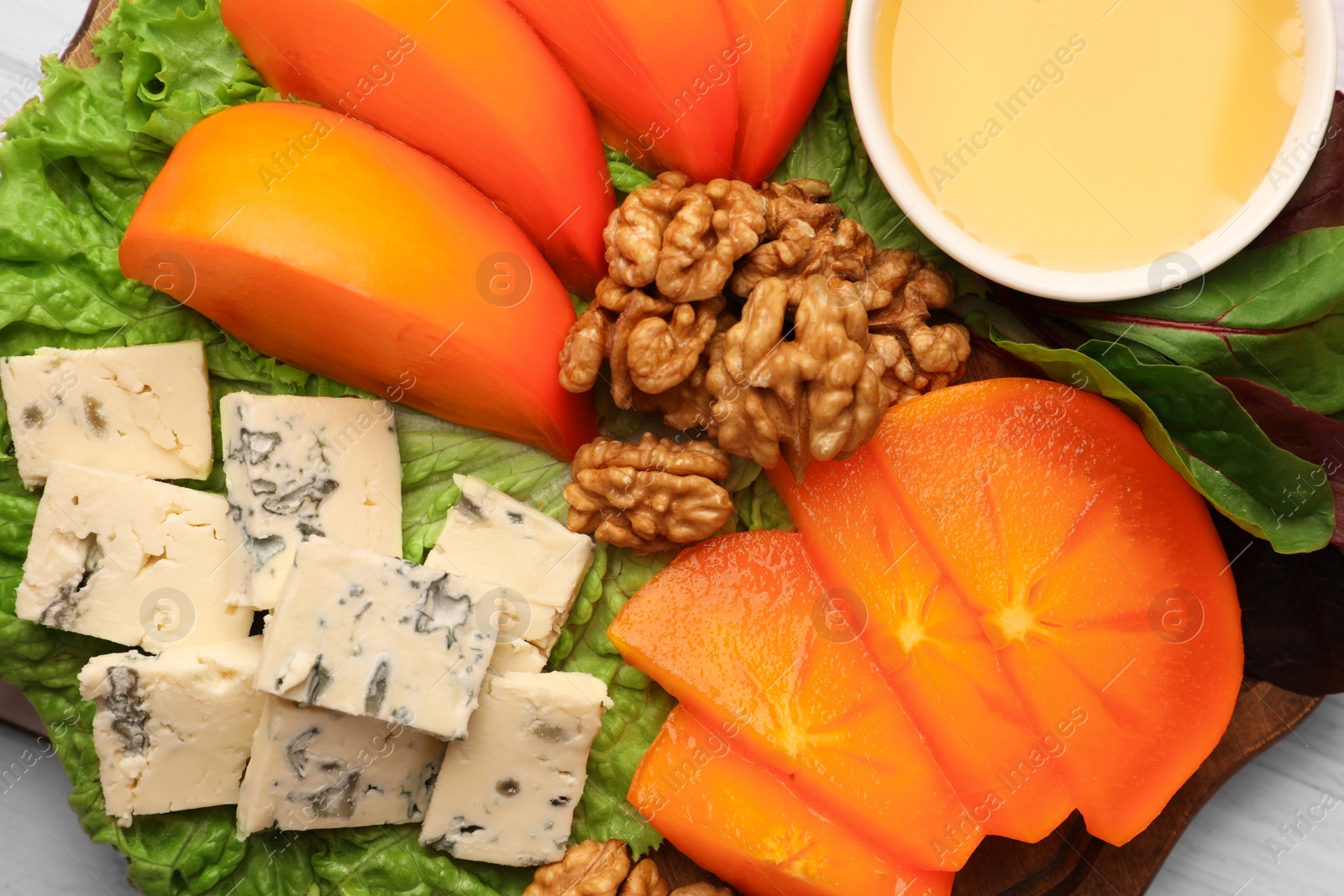 Photo of Delicious persimmon, blue cheese, nuts and honey served on white wooden table, flat lay