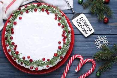 Traditional Christmas cake decorated with rosemary and cranberries on blue wooden table, flat lay
