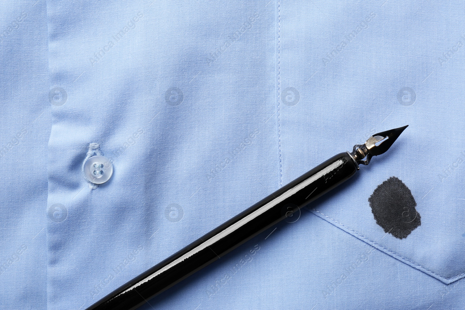 Photo of Black ink stain on light blue shirt and pen, top view. Space for text