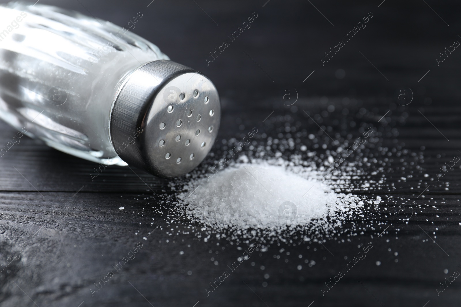 Photo of Organic salt in glass shaker on black wooden table, closeup