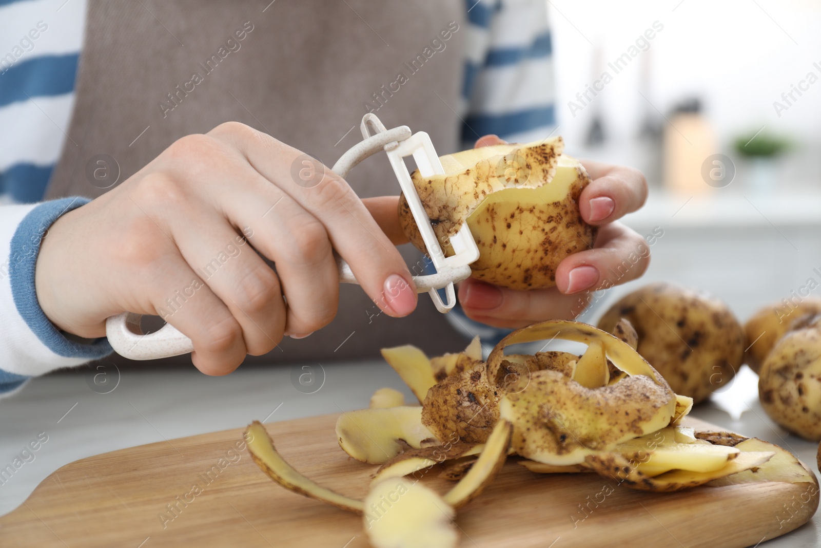 Photo of Woman peeling fresh potato at white table, closeup