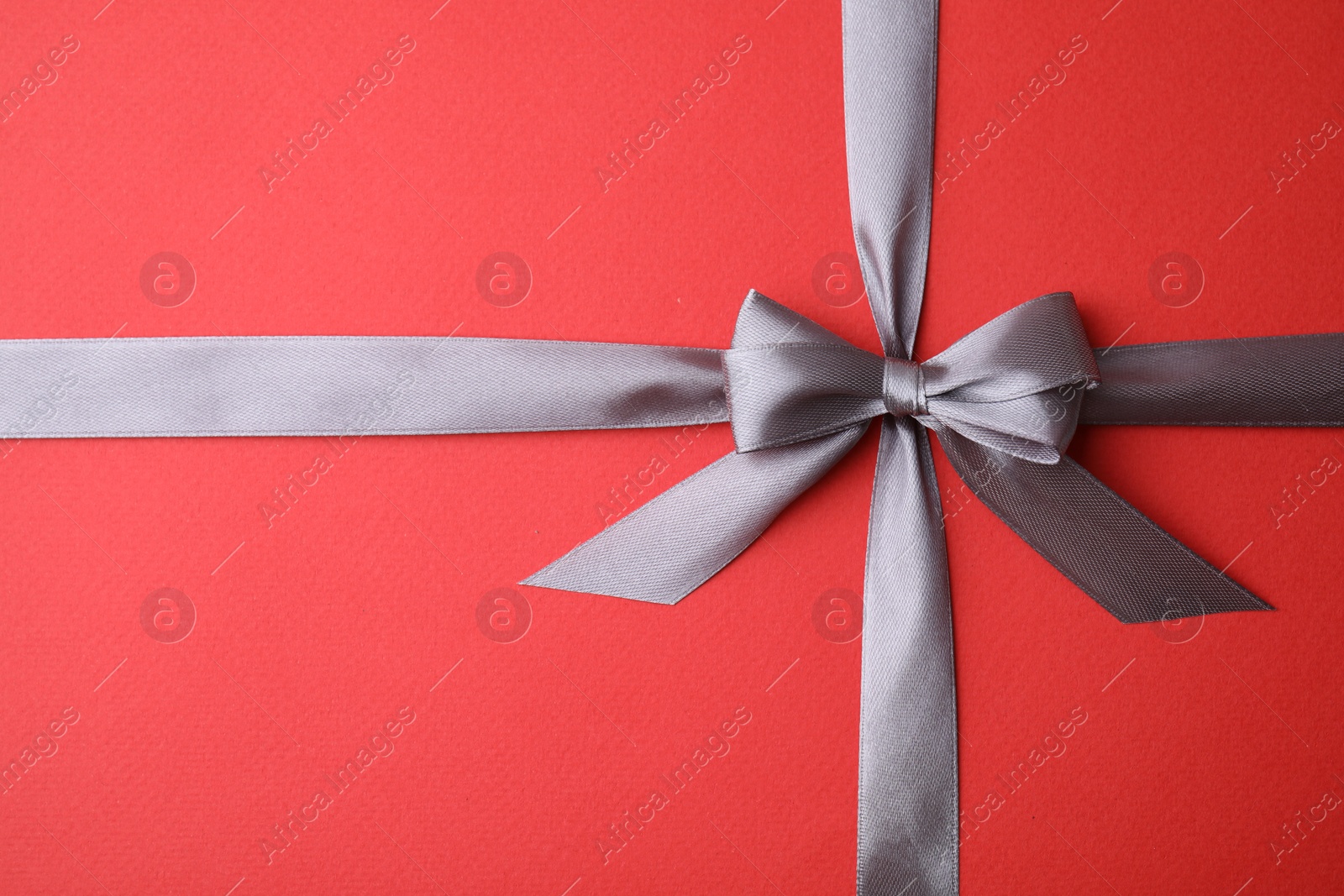 Photo of Grey satin ribbon with bow on red background, top view