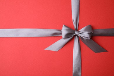 Grey satin ribbon with bow on red background, top view