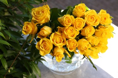 Photo of Beautiful bouquet of yellow roses in glass vase on white table outdoors, above view