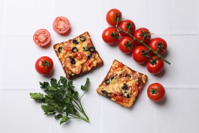 Tasty pizza toasts, fresh tomatoes and parsley on white tiled table, flat lay