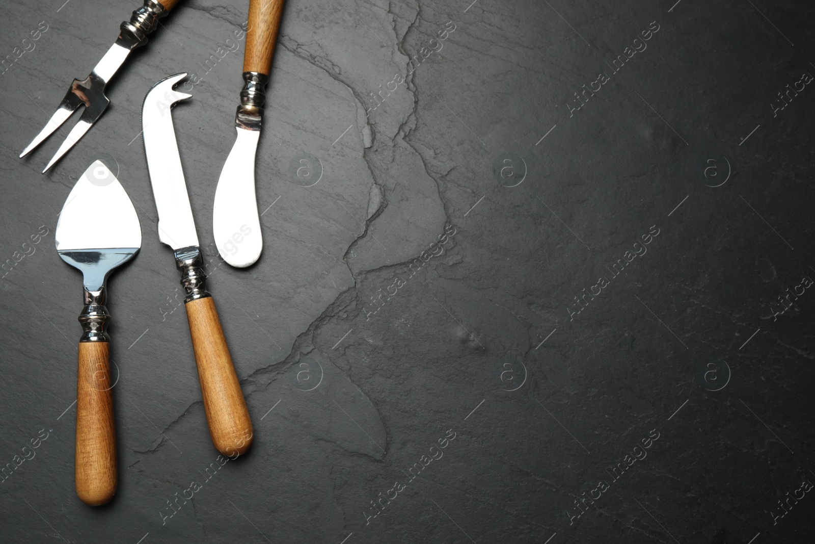 Photo of Cheese knives and fork on black stone table, flat lay. Space for text