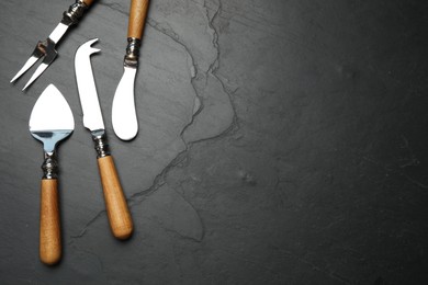 Cheese knives and fork on black stone table, flat lay. Space for text