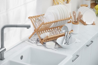 Sink and drying rack with clean dishes and cutlery on countertop in kitchen