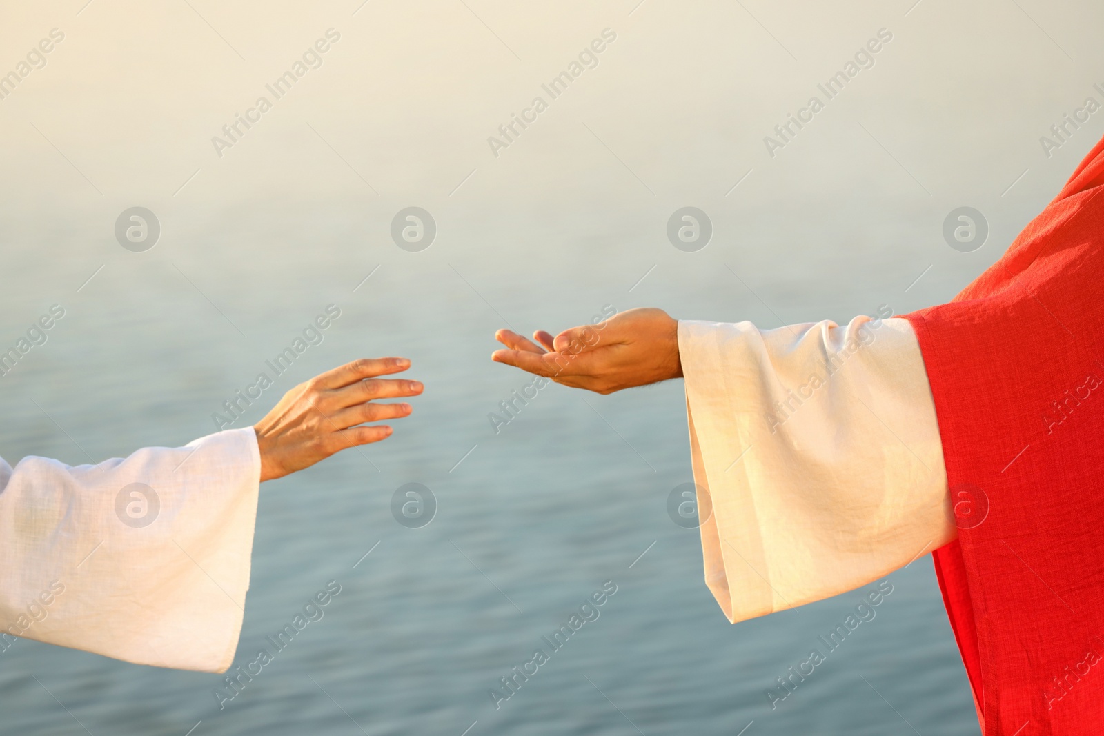 Photo of Woman reaching for Jesus Christ's hand near water outdoors, closeup