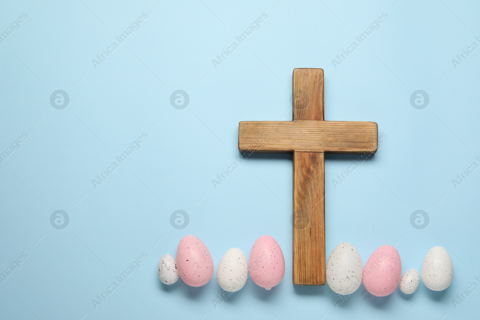 Photo of Wooden cross and painted Easter eggs on light blue background, flat lay. Space for text