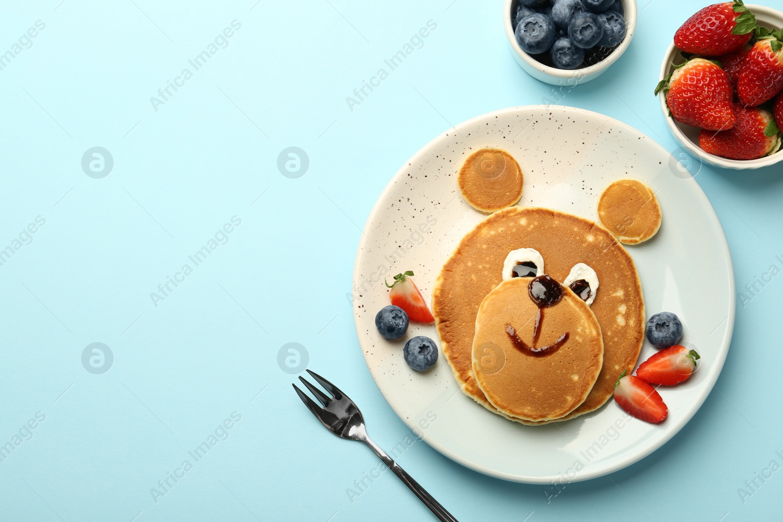 Photo of Creative serving for kids. Plate with cute bear made of pancakes and berries on light blue table, flat lay. Space for text