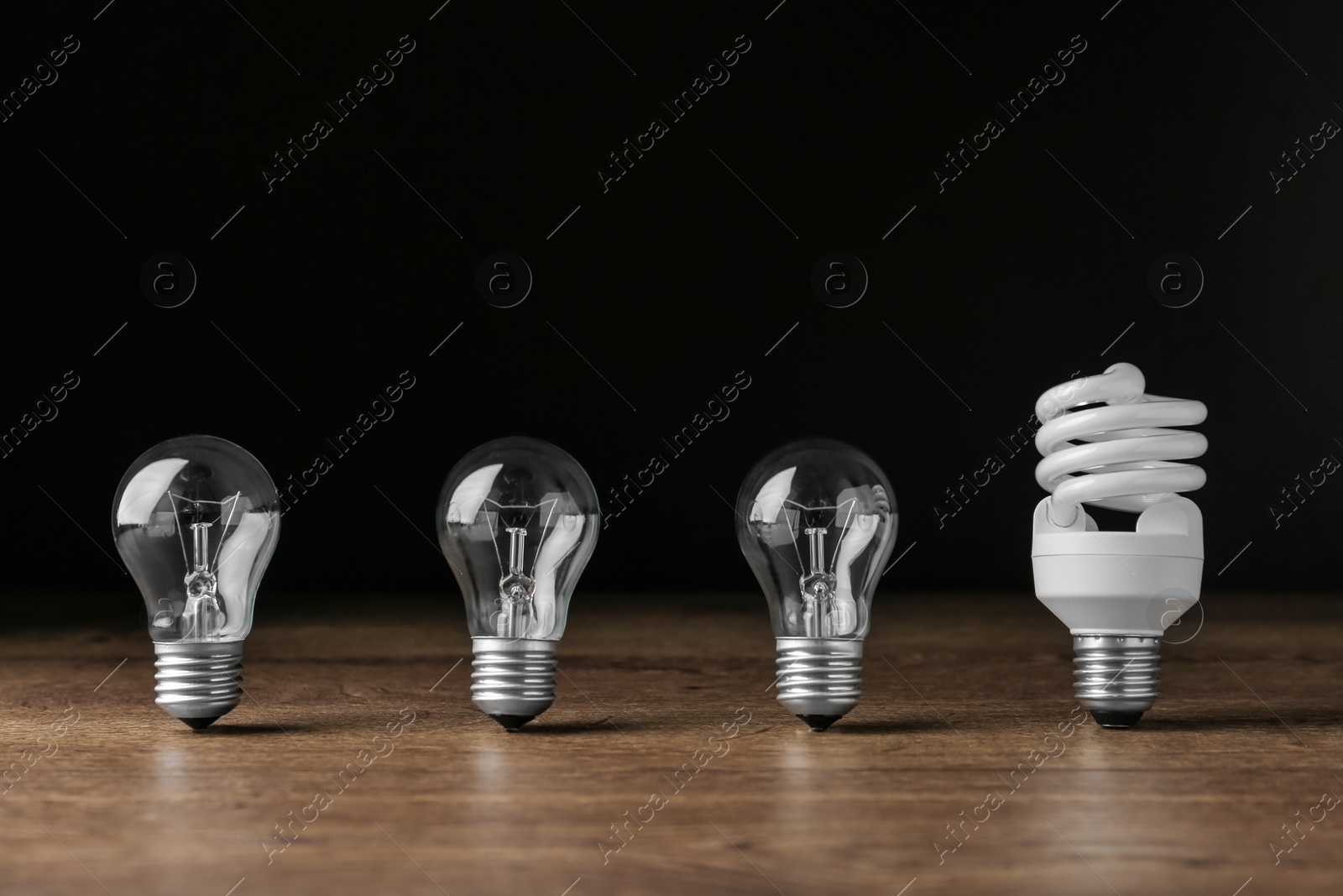 Photo of Fluorescent and incandescent lamp bulbs on wooden table against black background