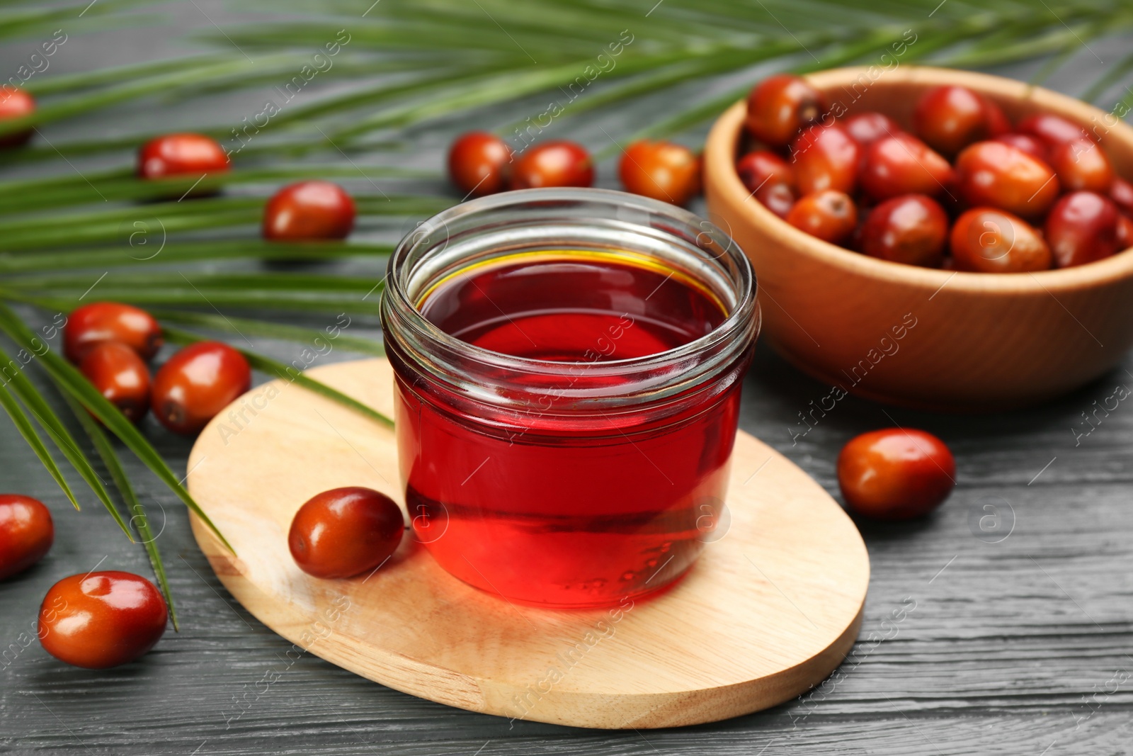 Photo of Palm oil in glass jar, tropical leaves and fruits on grey wooden table