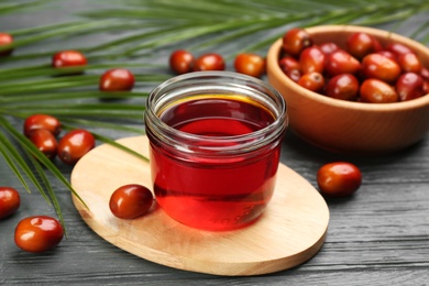 Palm oil in glass jar, tropical leaves and fruits on grey wooden table