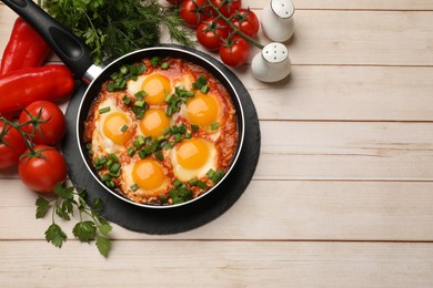 Flat lay composition with delicious shakshuka in frying pan on light wooden table. Space for text