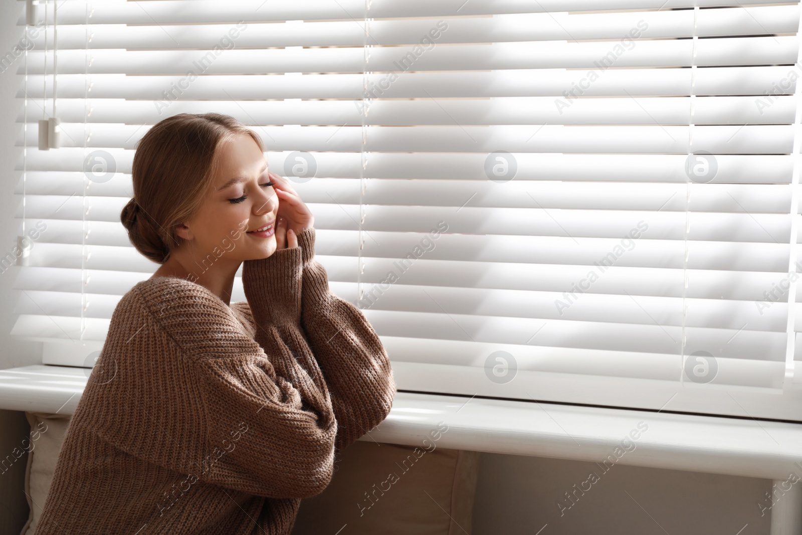 Photo of Beautiful young woman near window at home, space for text. Winter atmosphere