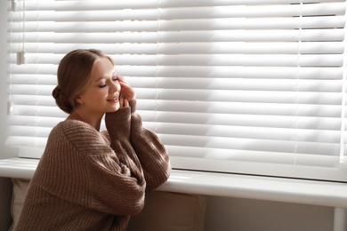 Beautiful young woman near window at home, space for text. Winter atmosphere