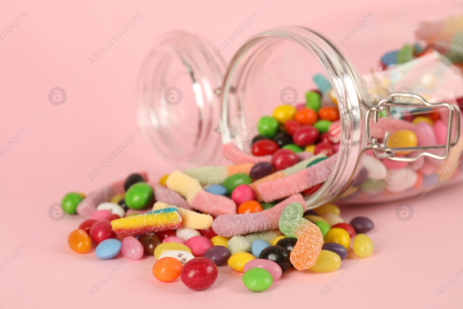 Photo of Overturned glass jar and scattered candies on pink background, closeup