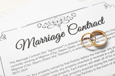 Photo of Marriage contract and gold rings on light wooden table, top view