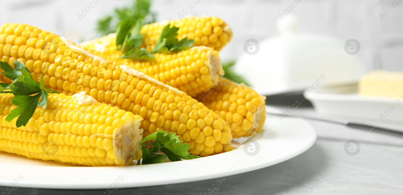 Image of Boiled corn cobs with butter and parsley on light grey table, closeup. Banner design