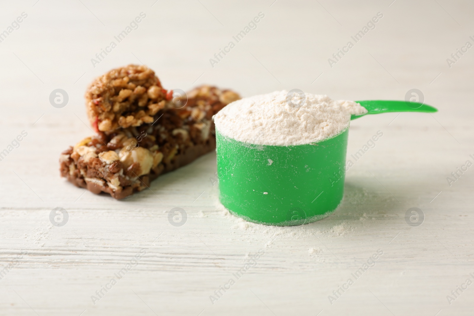 Photo of Tasty protein bars and scoop of powder on white table