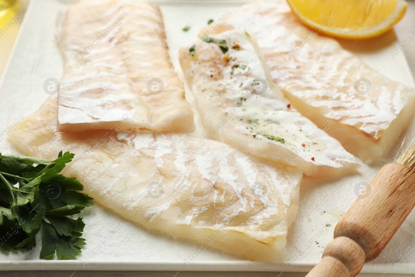 Photo of Fresh raw cod fillets with spices and brush on plate, closeup