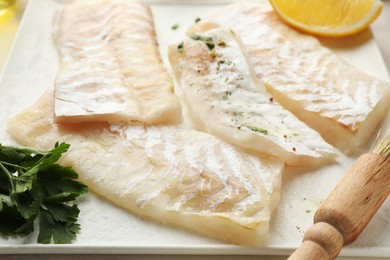 Photo of Fresh raw cod fillets with spices and brush on plate, closeup