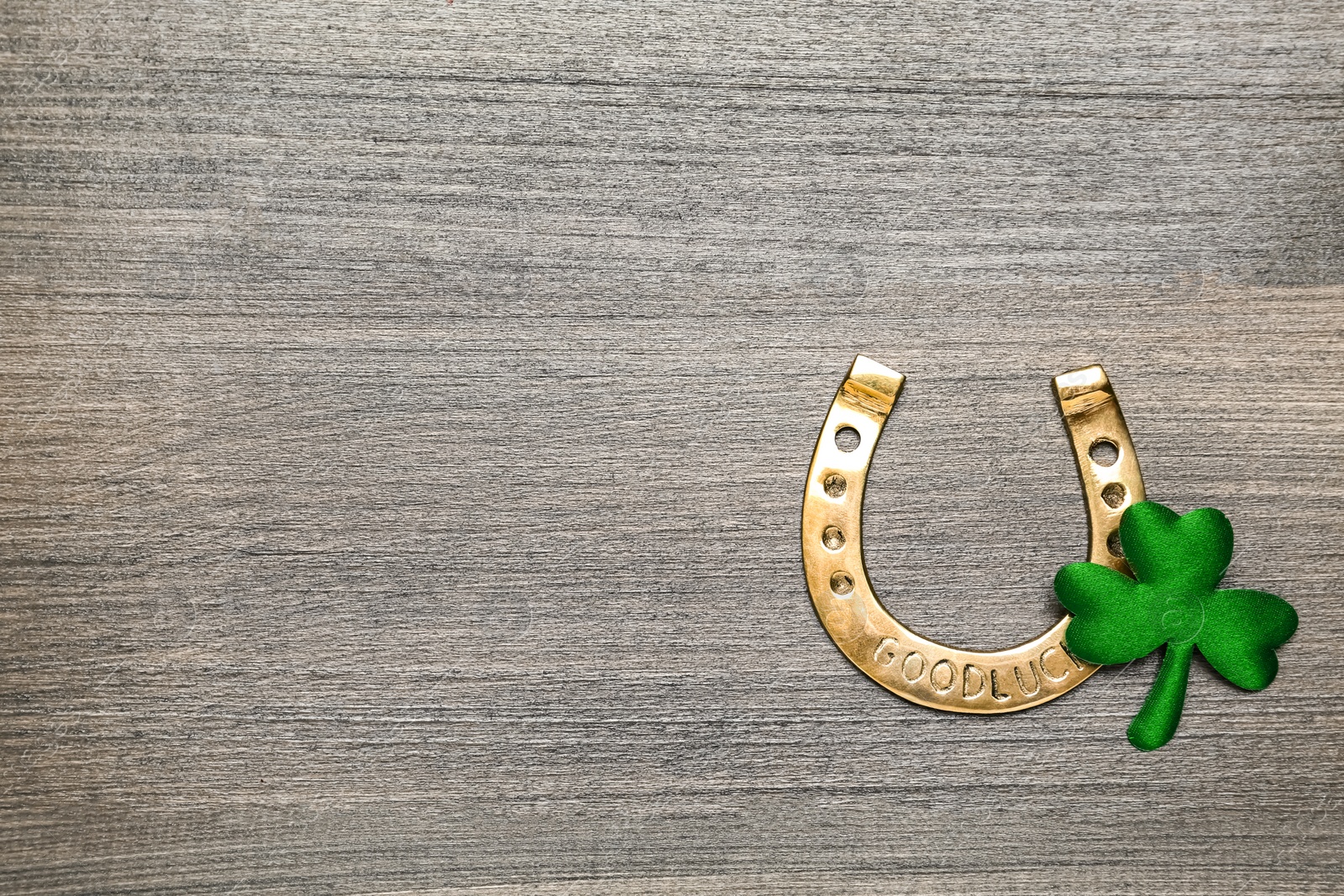 Photo of Golden horseshoe and decorative clover leaf on grey wooden table, flat lay with space for text. Saint Patrick's Day celebration