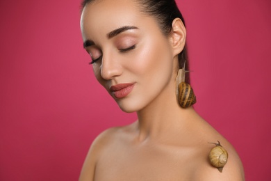 Photo of Beautiful young woman with snails on her body against pink background