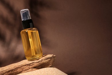 Photo of Bottle of serum and tree bark on sand against brown background. Space for text