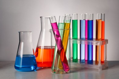 Different laboratory glassware with colorful liquids on wooden table against grey background