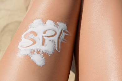 Woman with abbreviation SPF of sunscreen on leg at beach, closeup