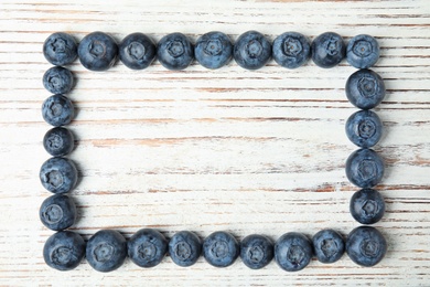 Frame made with fresh blueberries on white wooden table, top view. Space for text